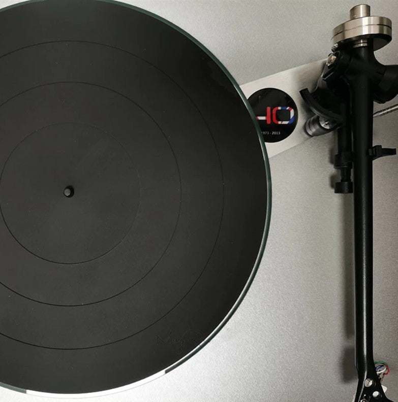 Close-up of a black rubber turntable platter mat and part of the tonearm on a light gray surface.